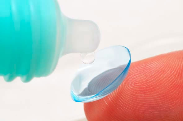 A closeup of a contact lens on a fingertip with a contact lens solution bottle