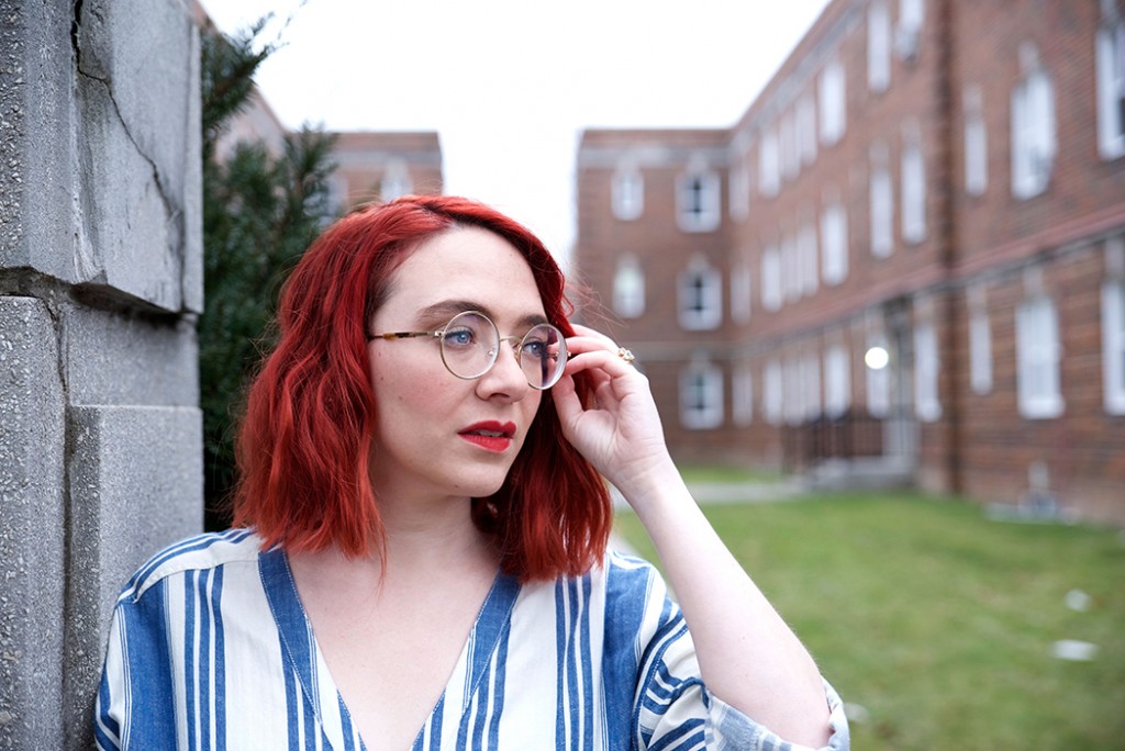 A woman with bright red hair and blue eyes wearing eyeglasses