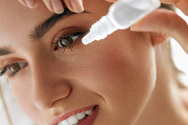 woman removes contact lenses and flushes her eyes with artificial tears or lubricating drops after water gets in her contacts when swimming