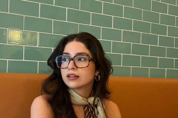 woman sitting at a booth wearing oversized glasses and a scarf tied around her neck