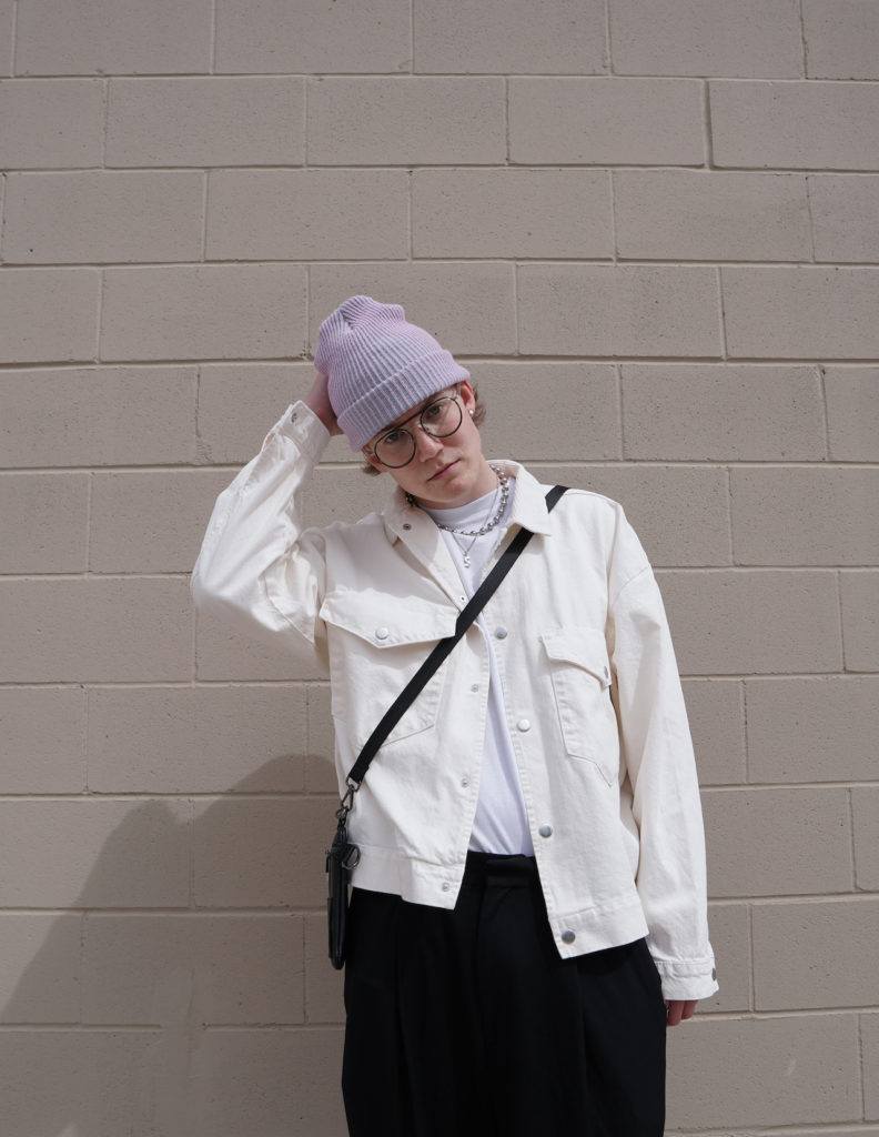 man wearing a light purple toque, a white jacket and aviator glasses, holding his hat