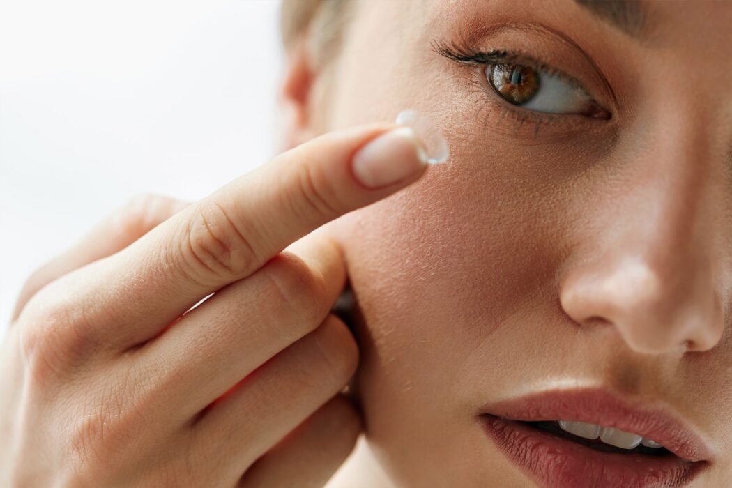 A woman with brown/amber eyes putting in a contact lens