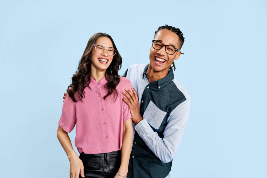 A smiling man and woman wearing eyeglasses in front of a light blue background